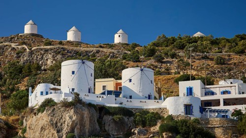Traditional white windmills on a hill surrounded by Mediterranean architecture and vegetation,