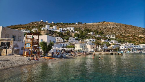 Beach promenade on a clear blue sea, behind it Mediterranean town and windmills on hill, Pandeli