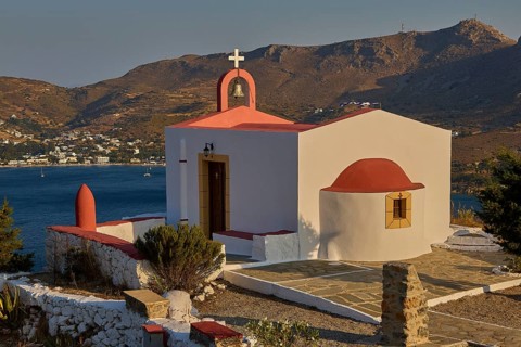 Chapel with red roof by the sea, surrounded by mountains and coastline, peaceful atmosphere,