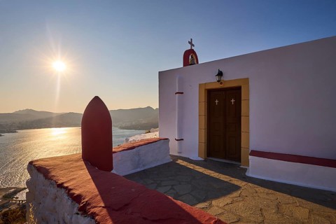 Chapel with cross by the sea at sunset, peaceful atmosphere and classic Greek architecture, red