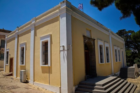 Yellow building with flag, surrounded by trees. Historic architecture with white window frames,