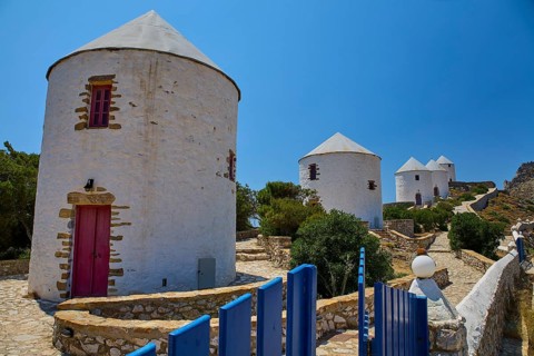 White windmills with red doors and fence under a blue sky on a sunny island, Pandeli Castle,