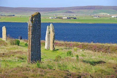 Ancient stones at the edge of a blue lake with green hills in the background, Ring of Brodgar,