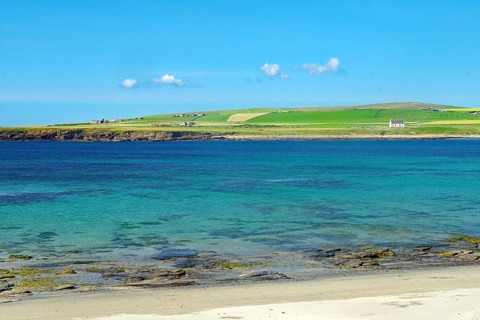 Clear blue sky over a coastal landscape with green shore and crystal clear water, Skara Brae,