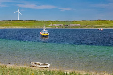 Colourful coastal landscape with boat, windmill and vast water under blue sky, Lambholm, Orkney