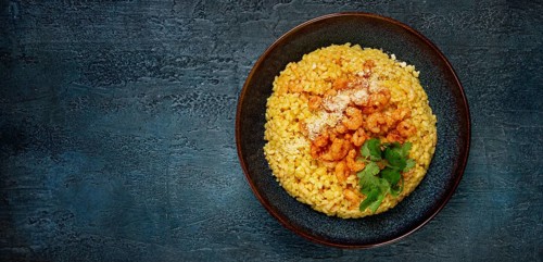 Risotto with shrimp, in a bowl, on a textured surface, with a side dish of fresh coriander,