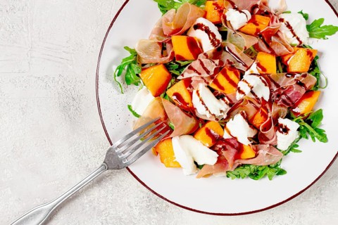 Salad with slices of ripe melon, prosciutto, mozzarella and fresh arugula, decorated with balsamic