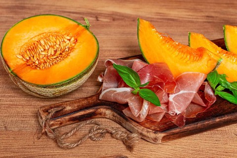 Cantaloupe melon, with prosciutto, and fresh basil, on a wooden serving board, rustic style