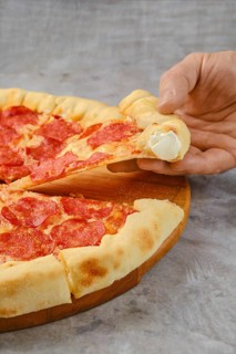 Delicious pepperoni pizza on a wooden board with a hand reaching for a slice. The crust is golden
