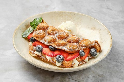 Colorful bubble waffles are served with fresh strawberries and blueberries, topped with creamy
