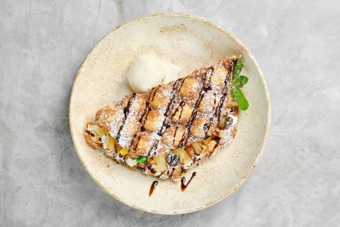 A beautifully plated dessert showcases a waffle filled with a variety of fresh fruits, drizzled