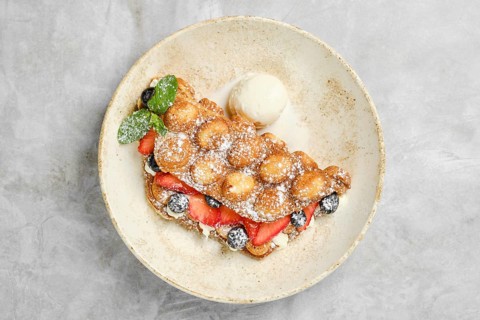 A golden bubble waffle is plated with strawberries, blueberries, and a scoop of vanilla ice cream.