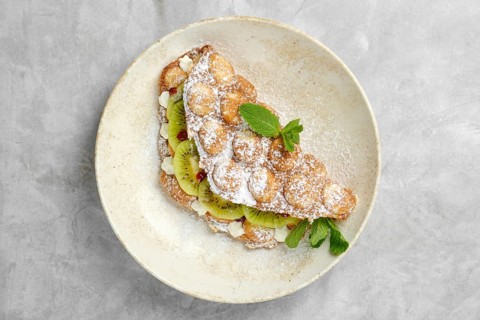 A delightful dessert featuring a crispy pastry shell filled with sliced kiwi, topped with powdered