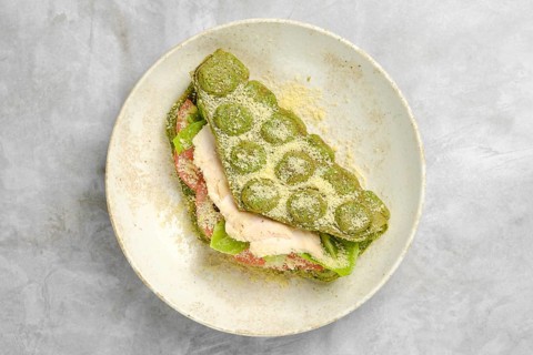A vibrant green wrap is layered with fresh lettuce, slices of tomato, and tender chicken, resting
