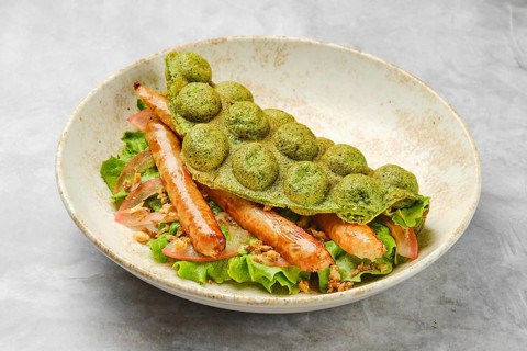 A vibrant green waffle is placed atop a bed of fresh lettuce, featuring tender grilled sausage and