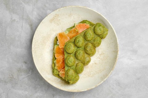 A unique green spinach waffle is folded over slices of smoked salmon, carefully arranged on a