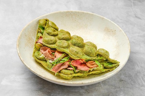 A matcha pancake showcases a vibrant green hue, folded elegantly with layers of savory ingredients