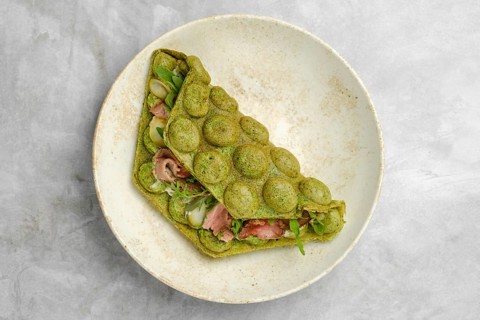 A green wrap made with spinach or herbs contains layers of fresh vegetables and meat, resting on a