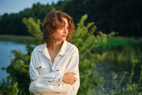 On a hot day, a woman stands near the calm lake, basking in the sunlight. Surrounded by lush