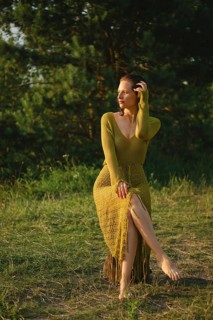 On a warm day, a woman sits gracefully by the lake surrounded by lush greenery. Wearing a fishnet