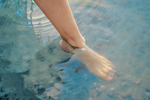 One foot dips into the refreshing lake water, creating gentle ripples on the surface. The bright