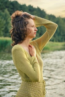 On a hot day, a woman stands gracefully by a serene lake touching her curly hair. She seems lost in