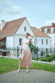 A stylish woman is posing gracefully in a lovely courtyard, dressed in a flowing pink dress. The