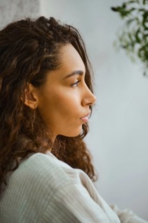 In a cozy indoor space, a woman with long, curly hair sits in profile, lost in thought. Soft