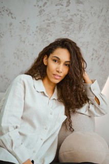 Charming woman with curly hair sits comfortably on a plush sofa in a contemporary indoor space.