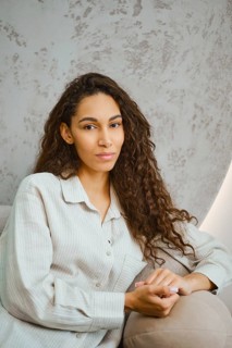 A young woman with long, curly hair is lounging on a sofa in a contemporary space. Soft afternoon
