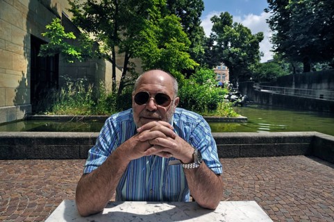 Portrait of an elderly gentleman with a beard and sunglasses sitting at a table, in the background