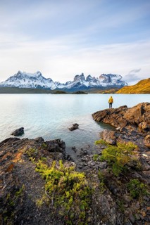 Young man on the shore of the blue lake Lago Pehoe in the evening light, Cuernos del Paine mountain