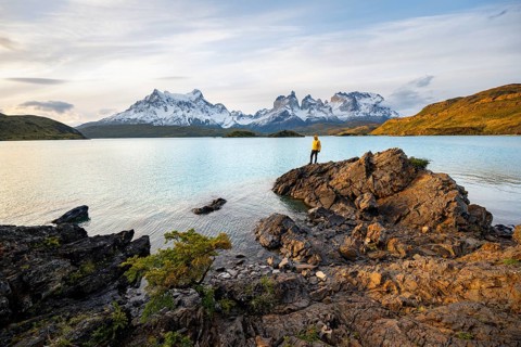 Young man on the shore of the blue lake Lago Pehoe in the evening light, Cuernos del Paine mountain