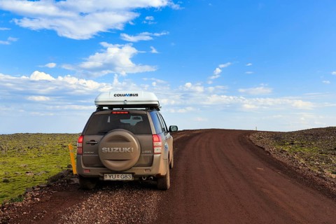 SUV Suzuki Grand Vitara with roof tent, travelling on a gravel road, Cumulus, Latrabjarg headland,