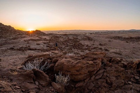 Photographer in desert landscape at sunrise with sun star, Erongo, Damaraland, Namibia