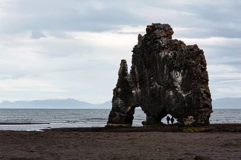 Tourists, couple at the basalt rock Hvitserkur, famous Elephant Rock at the lava beach, coastline,