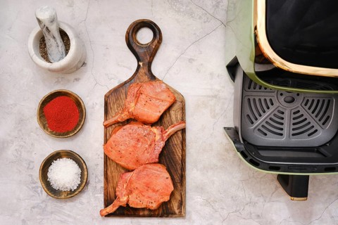 Three pork rib chops are placed on a wooden cutting board, surrounded by spices including paprika