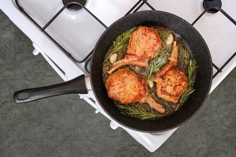 Pork rib roast sizzles in a skillet on the stovetop, surrounded by fragrant garlic and fresh herbs.