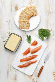 Herring caviar lay on a white cutting board beside a butter dish and sliced bread. Green dill adds