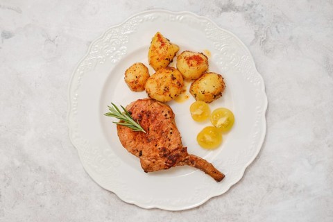 A roasted pork rib roast on a decorative white plate served with golden roasted potatoes and sweet