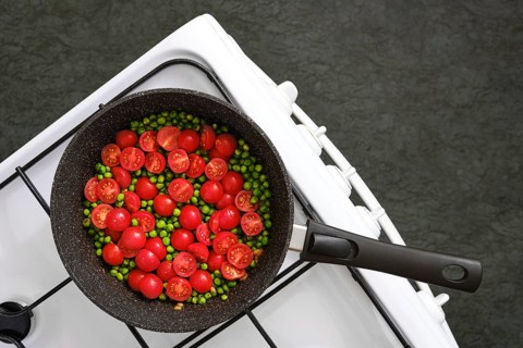 A skillet on a gas stove with red cherry tomatoes and green peas, cooking together in garlic butter