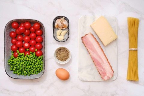 Overhead view of fresh cherry tomatoes, green peas, smoked bacon, garlic, parmesan cheese,