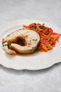 A generous portion of tender white fish is plated alongside a colorful mix of sautéed tomatoes and