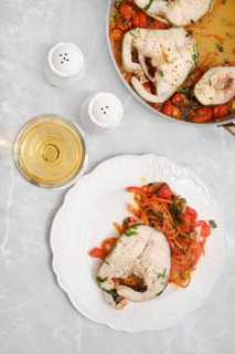 Tender cod fish fillet with colorful sautéed peppers, carrots and tomatoes on a plate on a dining