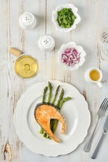 Grilled salmon and tender asparagus on a plate served for dinner. Bowls of chopped onion and herbs