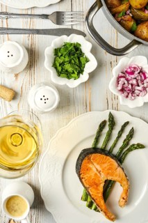 Salmon steak on a bed of asparagus, accompanied by fresh herbs and onions. A glass of white wine