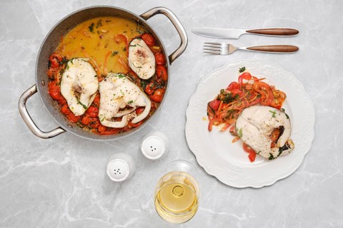 A flavorful fish dish is being prepared in a pot alongside a vibrant mix of tomatoes, carrots and