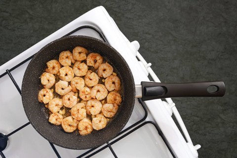 A frying pan on a stovetop filled with perfectly cooked shrimp in a kitchen. The shrimp are