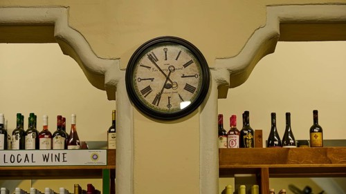 Agora, Municipal Market Hall, An antique clock on the wall of a wine shop with filled shelves, Kos