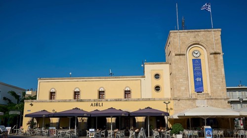 Cinema, Eleftherias Square, Historic building with clock tower and cafés under a blue sky, Kos